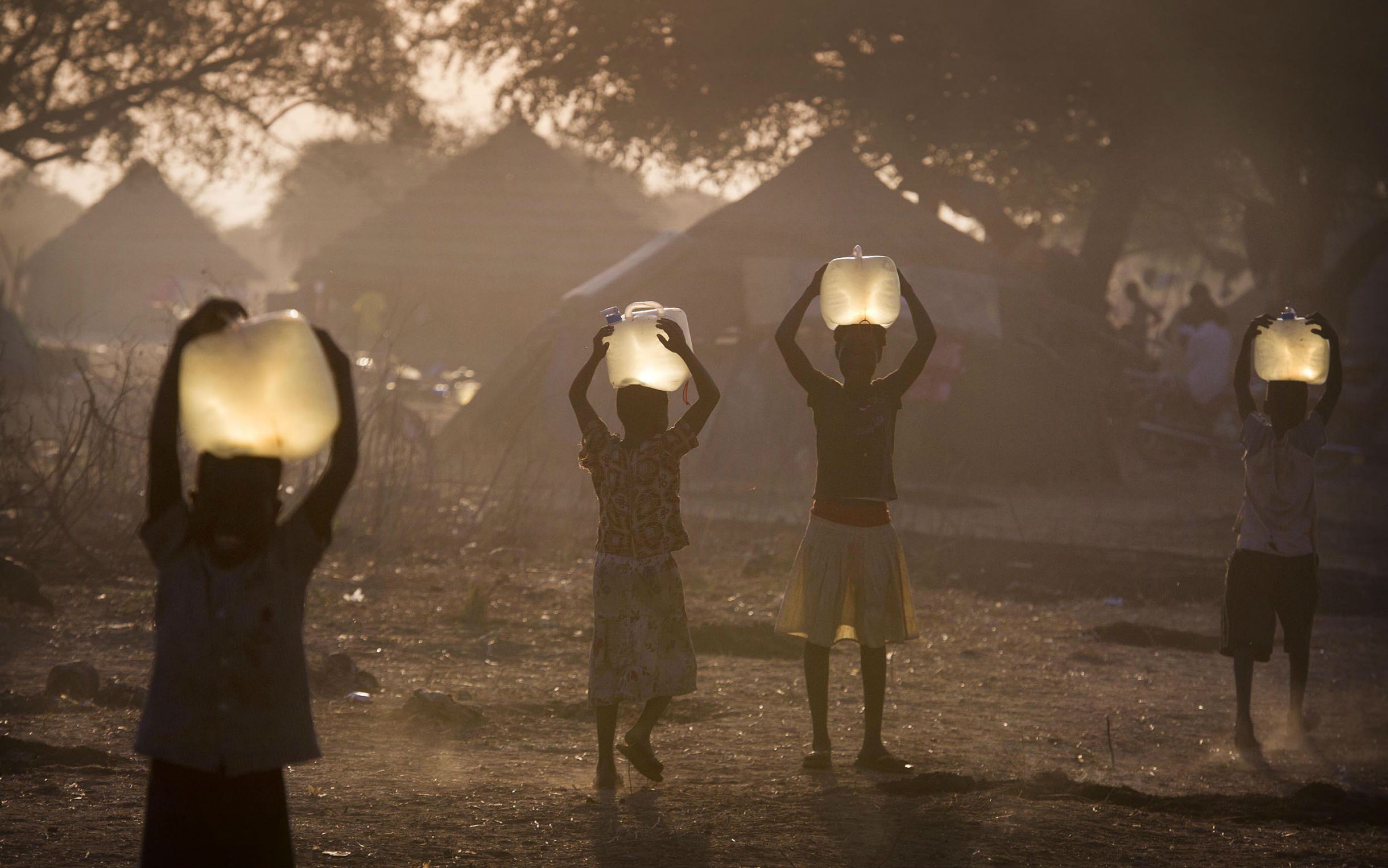 Children who have collected water bring it back to their temporary homes at the settlement in Awerial. Access to clean water for cooking and drinking significantly reduces the risk of waterborne diseases like cholera. Photo by Geoff Pugh/Oxfam