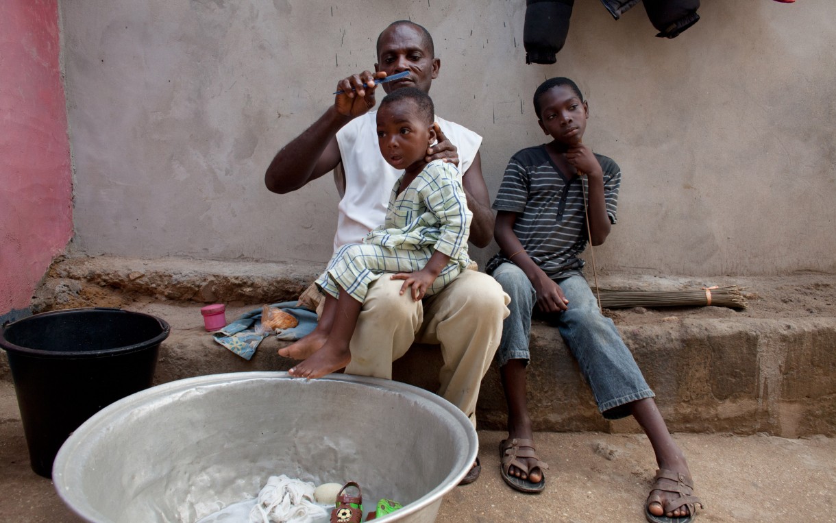 Steven Arthur finishes bathing and dressing his youngest son outside his home in Abuesi, Ghana. On days when Arthur is not at sea fishing, he takes charge of these household chores before he goes to work in the morning. Photo: Jane Hahn/Oxfam America