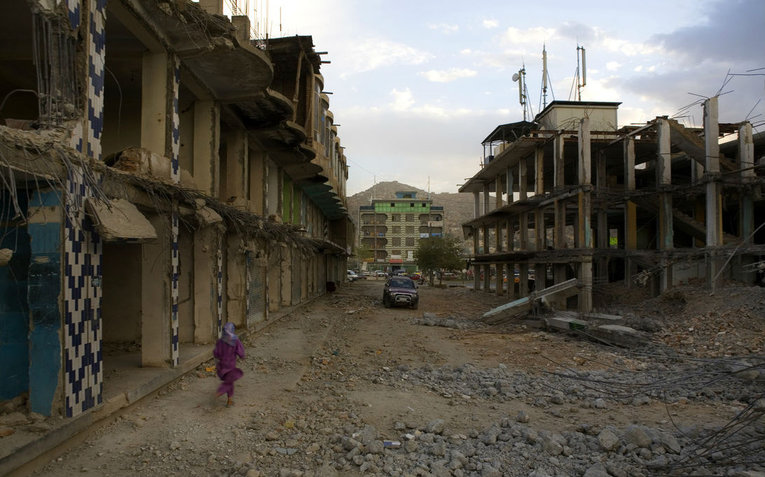 A young Afghan girl runs through ruined buildings. Photo: Travis Beard / Argus