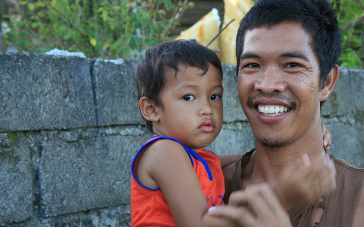 Rice Farmer Gorgonio Simborio holds his son Viran, age 3 in Leyte. He says, “Yolanda came just as we were about to harvest. Preparing our land for planting was delayed due to Yolanda coming and the money problems it caused us. I farm one hectare of land and it was badly damaged. I don’t own the land. I’m a tenant farmer. What harvest I get is always sold because we end up with debts. While we’re waiting for the harvest, we borrow from traders. At the moment we are relying on relief food. My wife is away in Manila working so we can get some kind of income. So for now I’m a single dad.” Photo: Jane Beesley / Oxfam