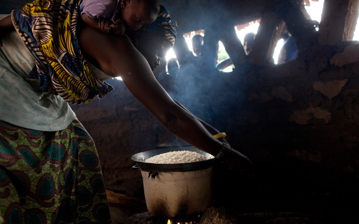 Karfa Mane begins to prepare rice for supper - with her granddaughter secured to her back - in the kitchen area of her home in Sare Dembara, Senegal. Photo: Holly Pickett / Oxfam America